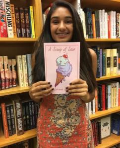 Young author, Sahana Singh, standing in front of bookshelves with a copy of her published novel titled A Scoop of Sour.